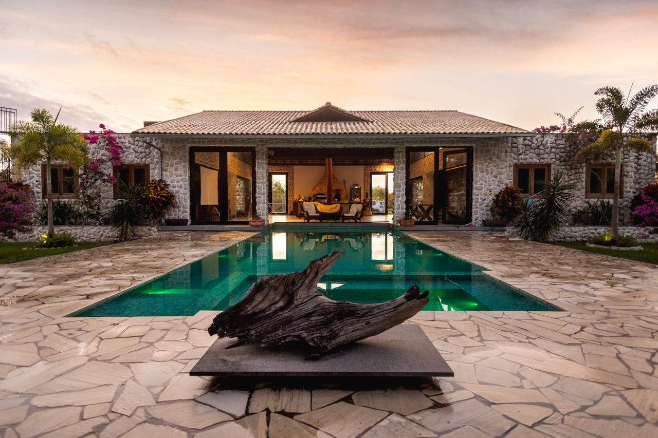 Elegant villa with a pool, stone facade, and tropical garden at sunset.
